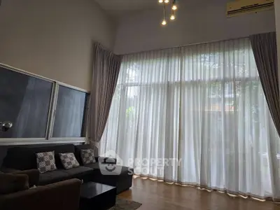Spacious living room with high ceilings and large windows, featuring elegant curtains and modern lighting.