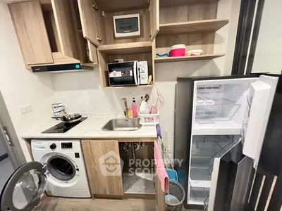 Compact kitchen with modern appliances including washing machine and open fridge.
