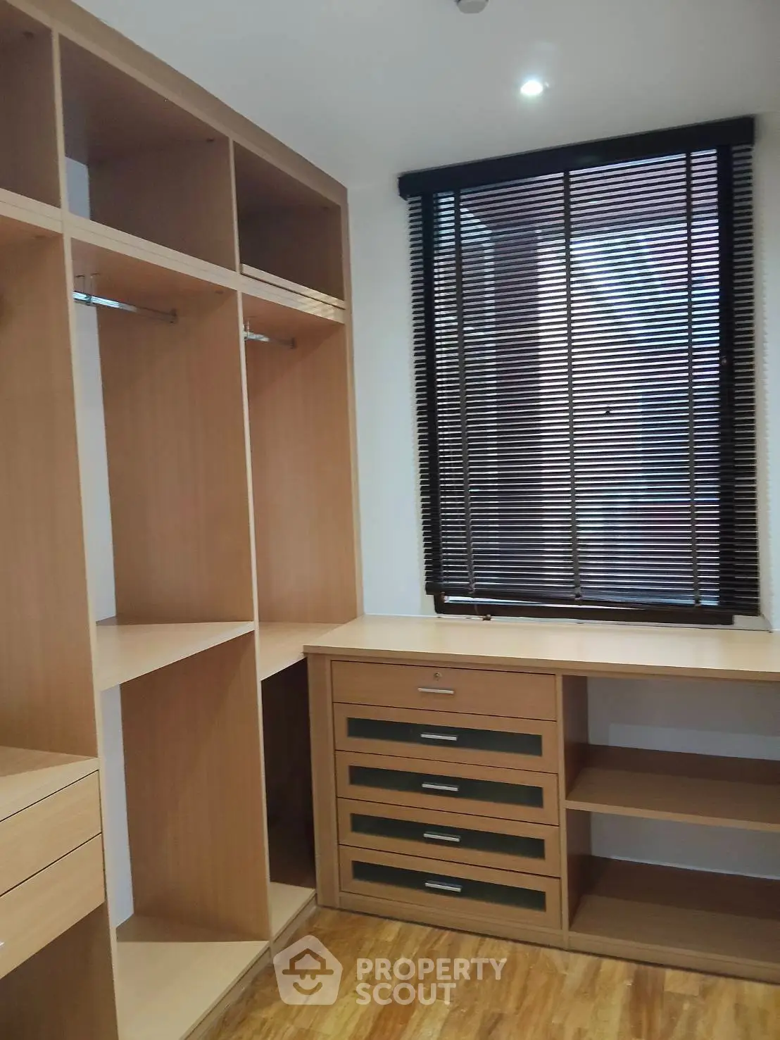 Spacious walk-in closet with wooden shelves and drawers, featuring natural light from window blinds.