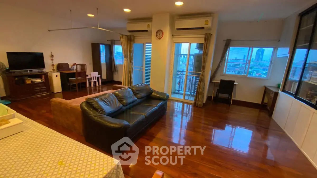 Spacious living room with polished wooden floors and city view balcony in modern apartment.