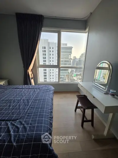 Modern bedroom with city view, featuring a stylish bed and vanity desk, perfect for urban living.