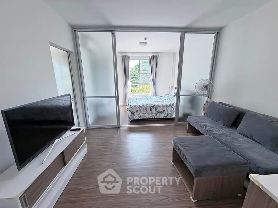Modern living room with sliding doors leading to a bright bedroom, featuring sleek furniture and a large window view.
