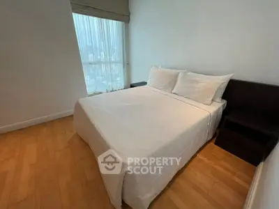 Cozy bedroom with wooden flooring and large window offering city views.