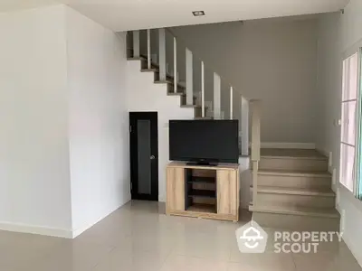 Modern minimalist living room with staircase and sleek TV stand, perfect for cozy entertainment and relaxation.