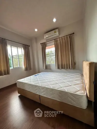 Spacious bedroom with large windows and natural light, featuring a comfortable bed and elegant curtains.