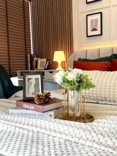 Cozy bedroom with stylish decor, featuring a plush bed, elegant lamp, and decorative books for a warm ambiance.