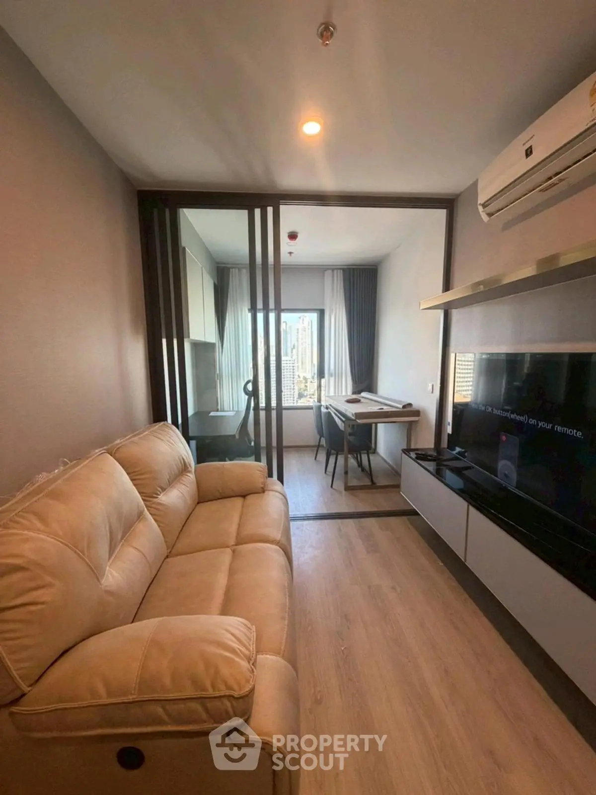 Modern living room with beige sofa and city view from window.