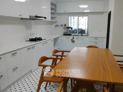 Modern kitchen with sleek white cabinets and wooden dining table, featuring a gas stove and stylish chairs.