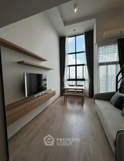 Modern living room with high ceiling and large windows offering city views, featuring sleek wooden shelves and cozy seating.