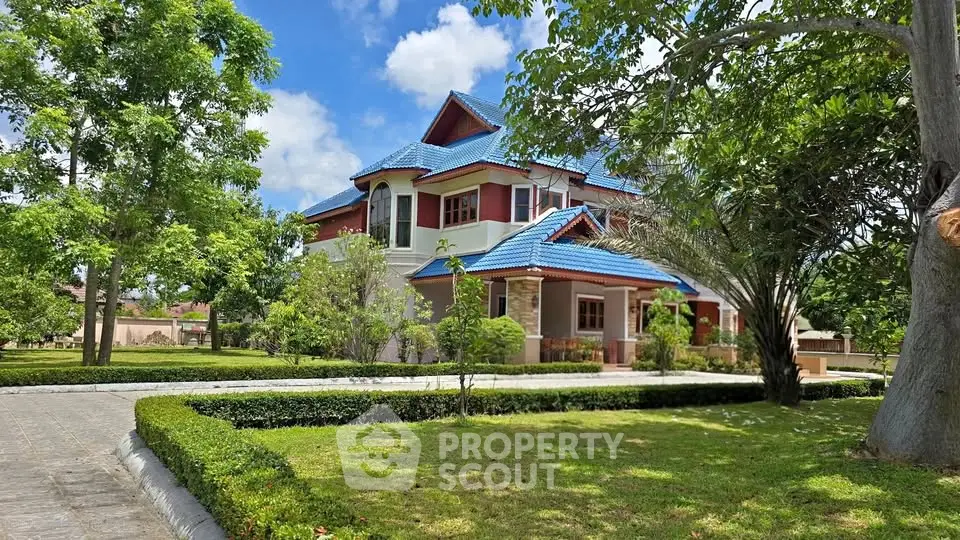 Stunning two-story house with blue roof surrounded by lush greenery and manicured garden.