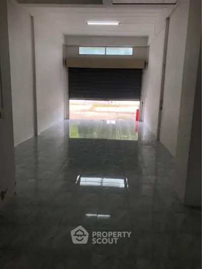 Spacious commercial space with glossy tiled flooring and large roller shutter door.