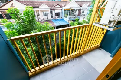 Charming balcony with vibrant yellow railing overlooking lush greenery and residential street.