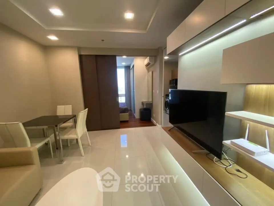 Modern living room with sleek furniture and open layout, featuring a large TV and dining area.