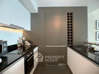 Modern kitchen with sleek cabinetry and built-in wine rack, featuring black countertops and stainless steel appliances.