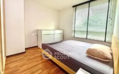 Cozy bedroom with wooden flooring and large window with blinds.