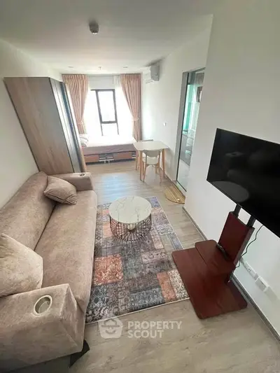 Modern living room with cozy sofa, stylish rug, and wall-mounted TV in a bright apartment.