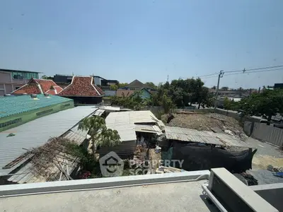 Urban view from balcony overlooking rooftops and construction site under clear blue sky.