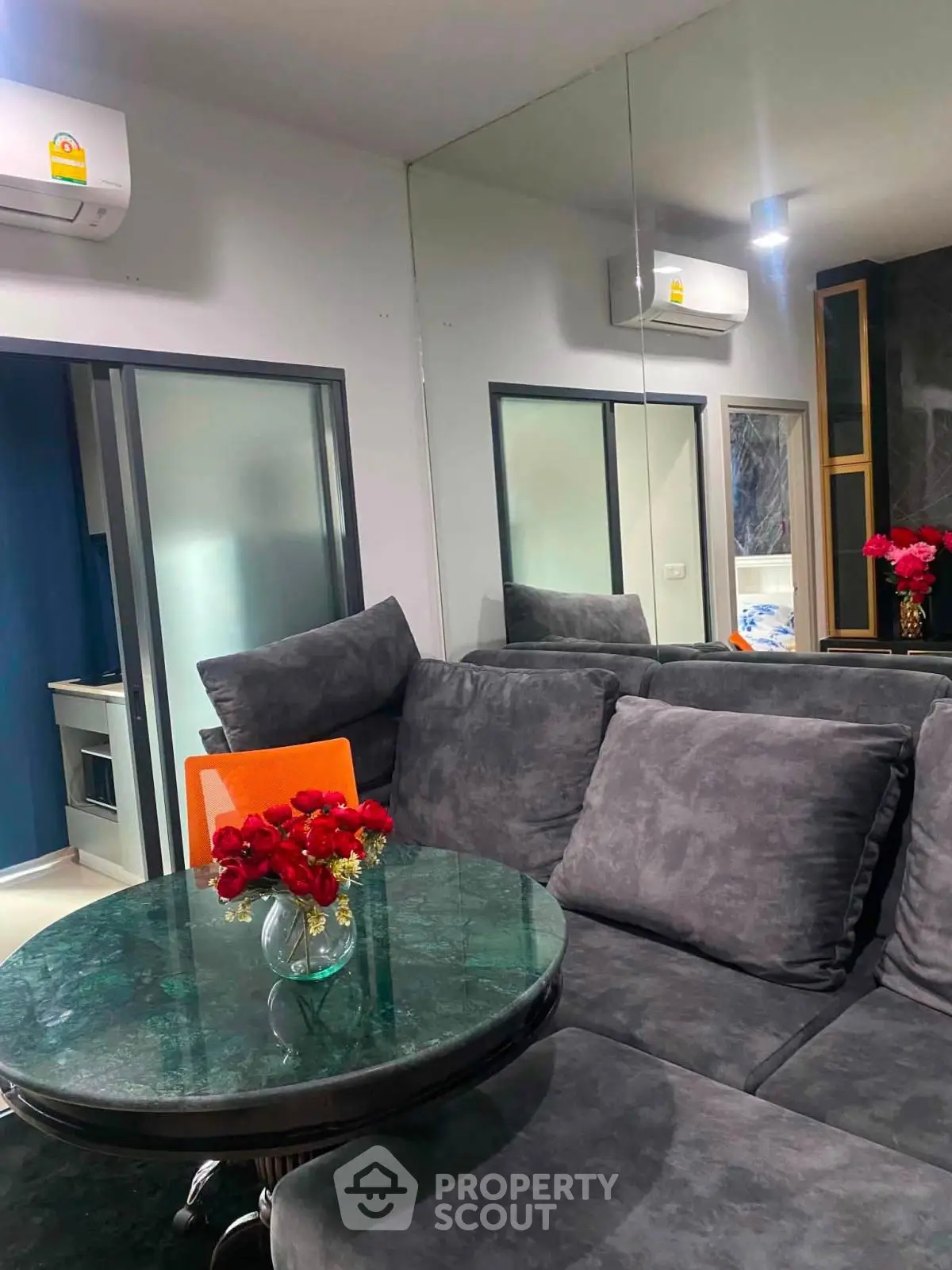 Modern living room with plush gray sofa and glass table, featuring elegant decor and air conditioning.