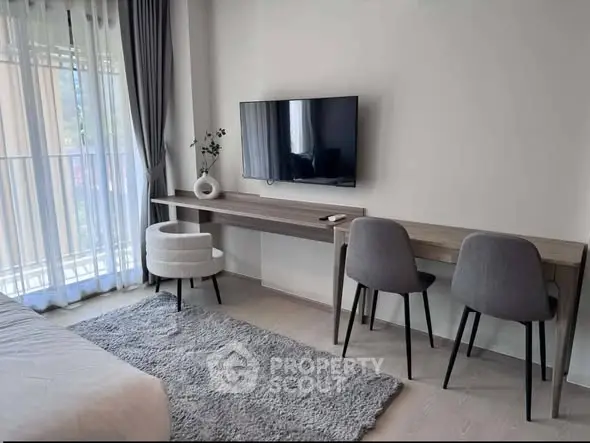 Modern living room with wall-mounted TV, stylish chairs, and natural light from large windows.