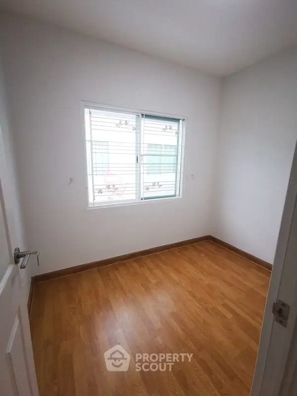 Bright empty room with wooden flooring and large window, perfect for customization.