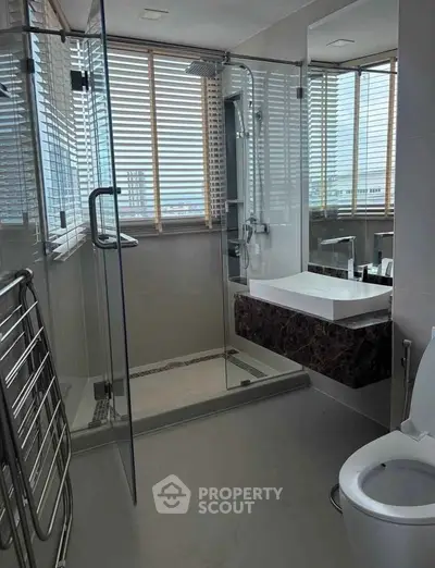 Modern bathroom with glass shower, sleek fixtures, and city view through large windows.
