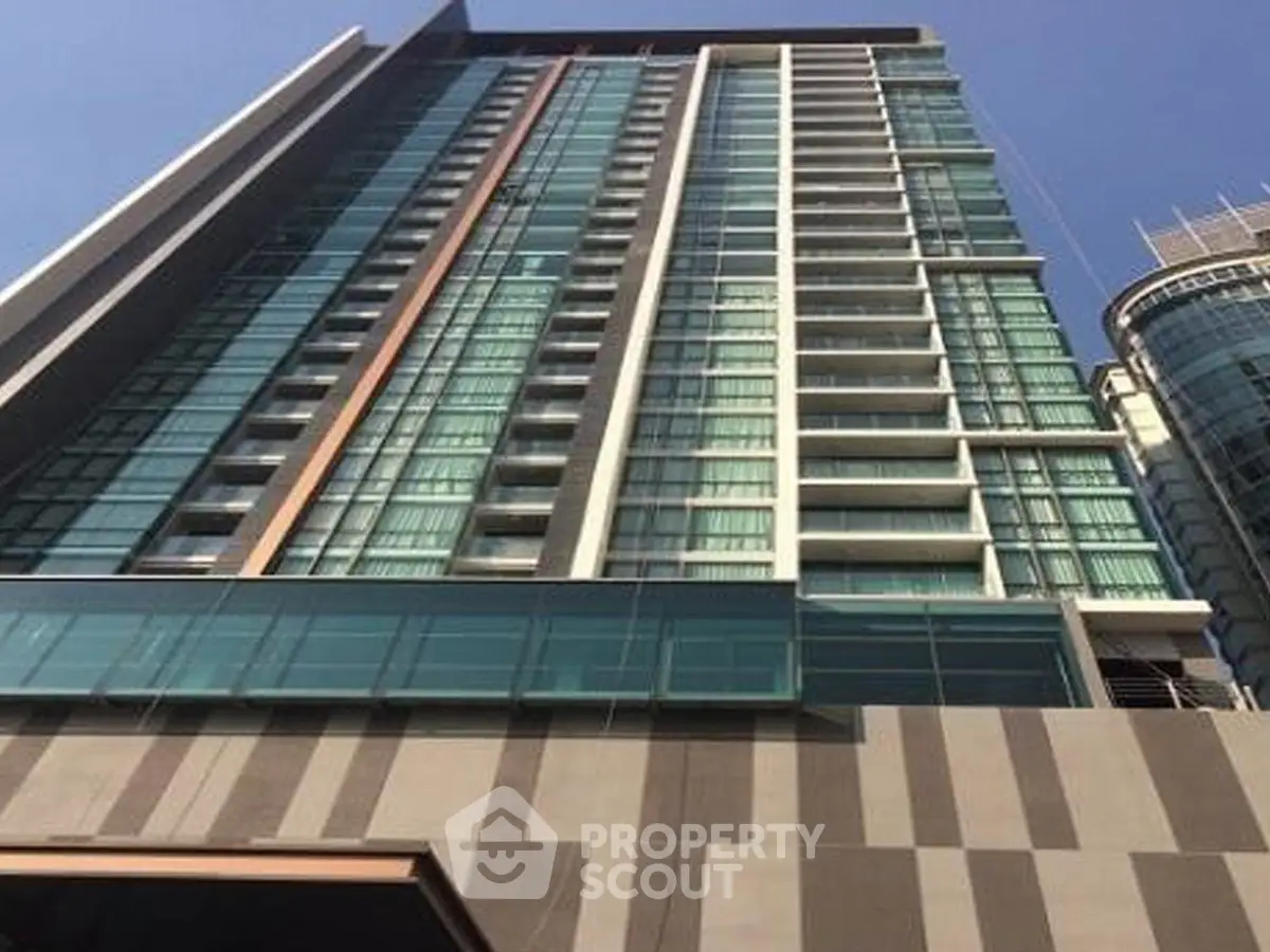 Modern high-rise building with glass facade and balconies in urban setting.