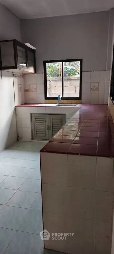 Charming kitchen with tiled countertops and natural light, perfect for culinary enthusiasts.