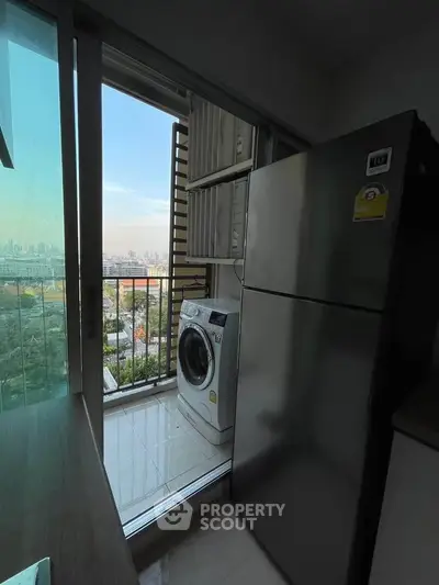 Compact kitchen with fridge and washing machine, offering a city view from the balcony.