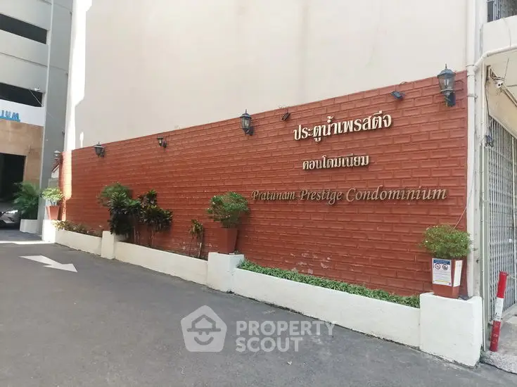 Patumwan Prestige Condominium entrance with brick wall and potted plants.