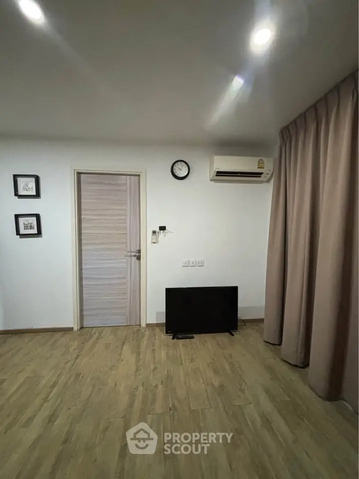 Modern living room with wooden flooring, wall-mounted air conditioner, and minimalist decor.