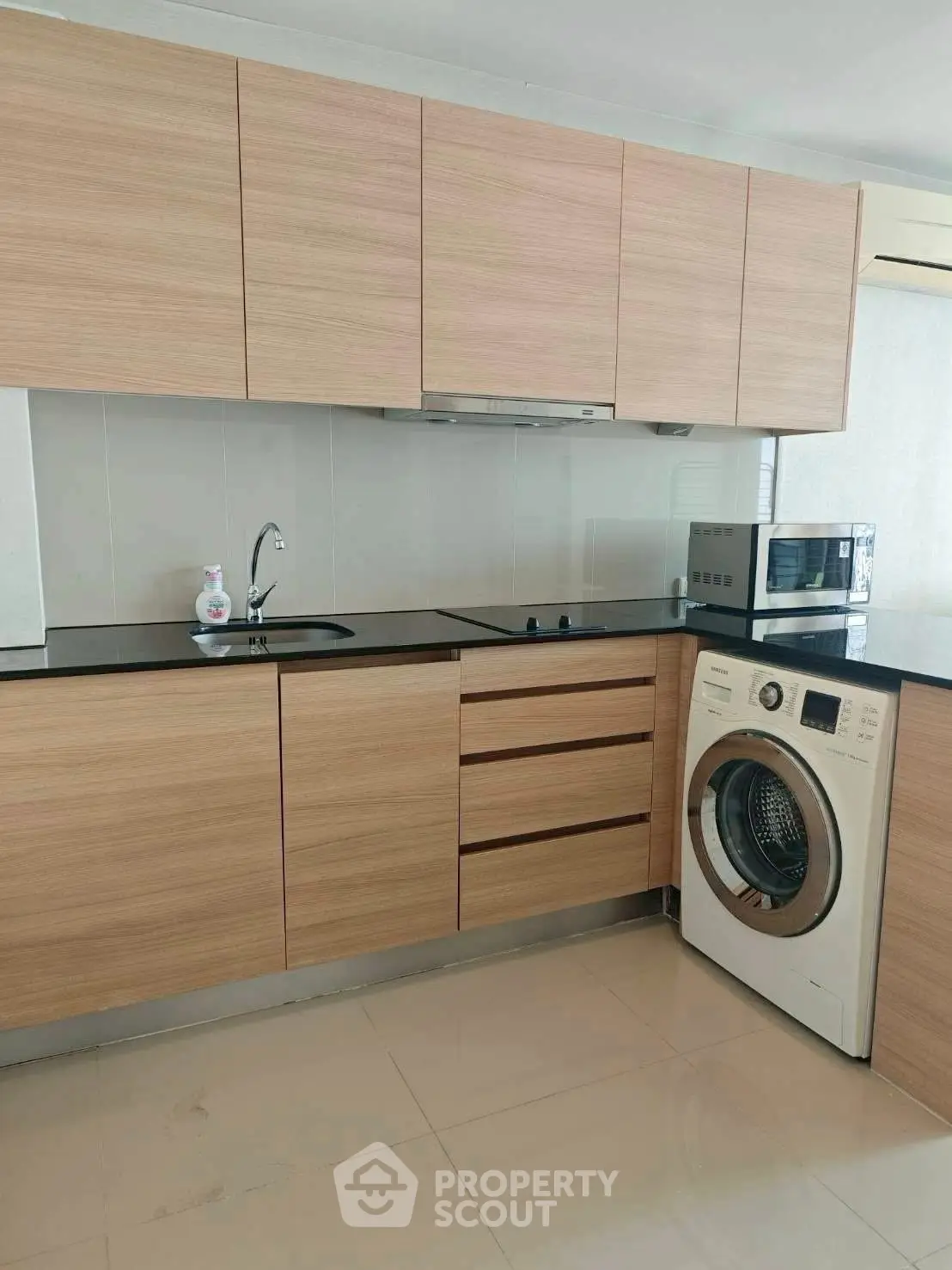 Modern kitchen with wooden cabinets, washing machine, and microwave in sleek apartment.