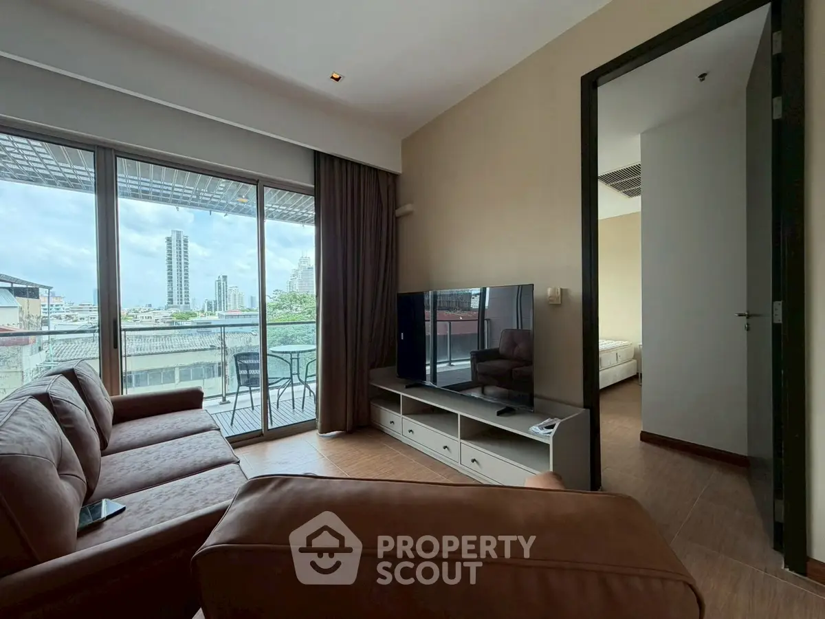 Spacious living room with leather sofa and large TV, opening to a balcony with city views.
