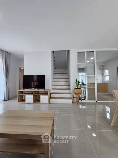 Modern living room with sleek staircase and open kitchen layout, featuring stylish furniture and natural light.