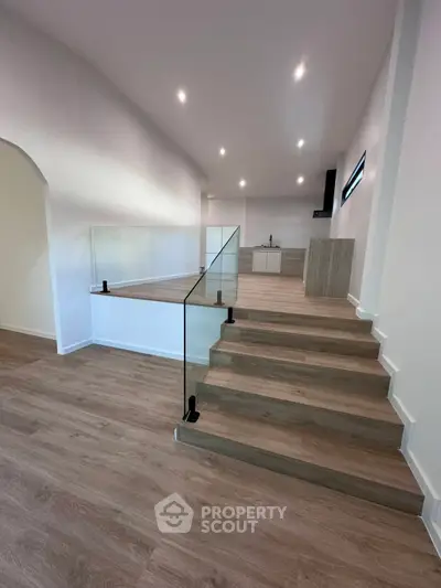 Modern open-plan living space with sleek glass railing and stylish wooden flooring.