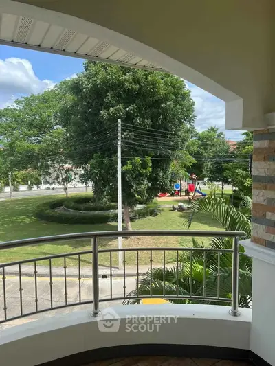 Charming balcony view overlooking lush green park with trees and clear blue sky.