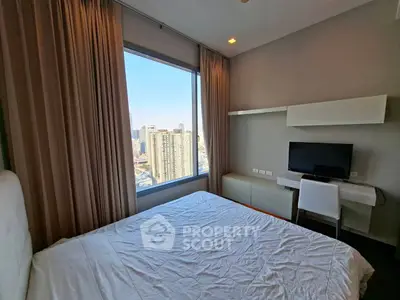 Modern bedroom with city view, featuring a large window, desk, and TV, perfect for urban living.
