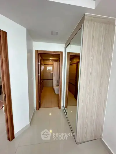 Modern hallway leading to a sleek bathroom with wooden accents and mirrored closet doors.