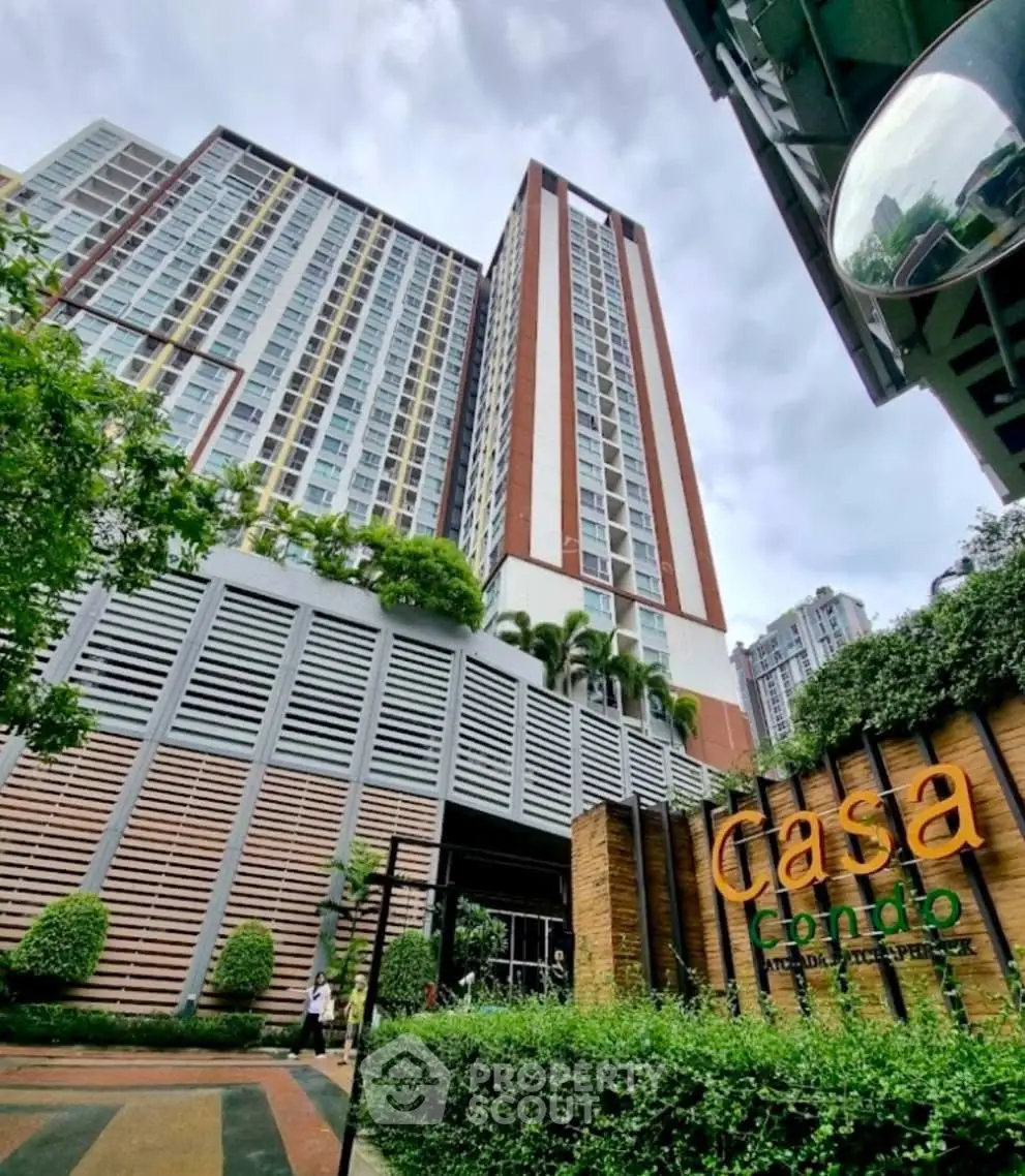 Modern high-rise condo building with lush greenery and stylish entrance signage.