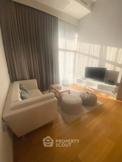 Modern living room with cozy seating and natural light, featuring a sleek TV setup and elegant wooden flooring.