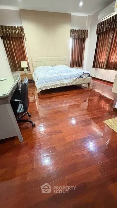 Spacious bedroom with polished wooden floors and elegant curtains.