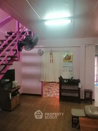 Cozy living room with wooden flooring and pink staircase, perfect for family gatherings.