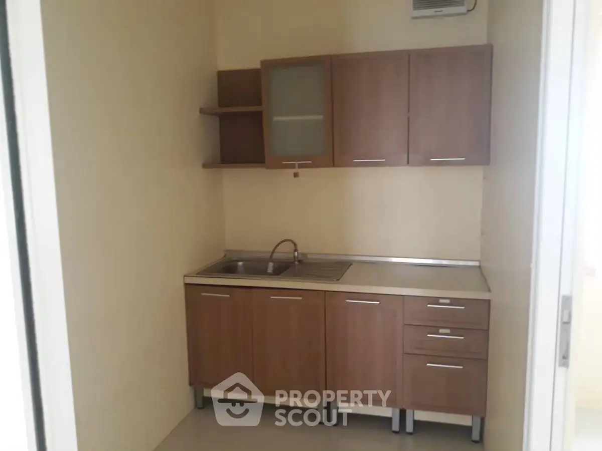 Compact kitchen with wooden cabinets and stainless steel sink in cozy apartment