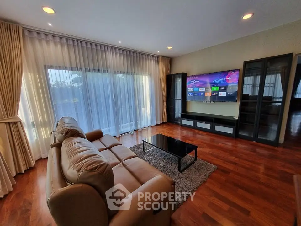 Spacious living room with modern decor and large TV, featuring elegant curtains and wooden flooring.