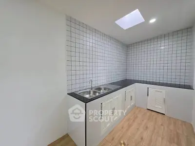 Modern kitchen with sleek white cabinetry and dual sink, featuring a skylight and tiled backsplash.