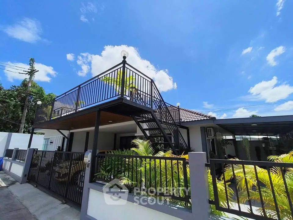 Modern house with rooftop terrace and lush garden under clear blue sky.