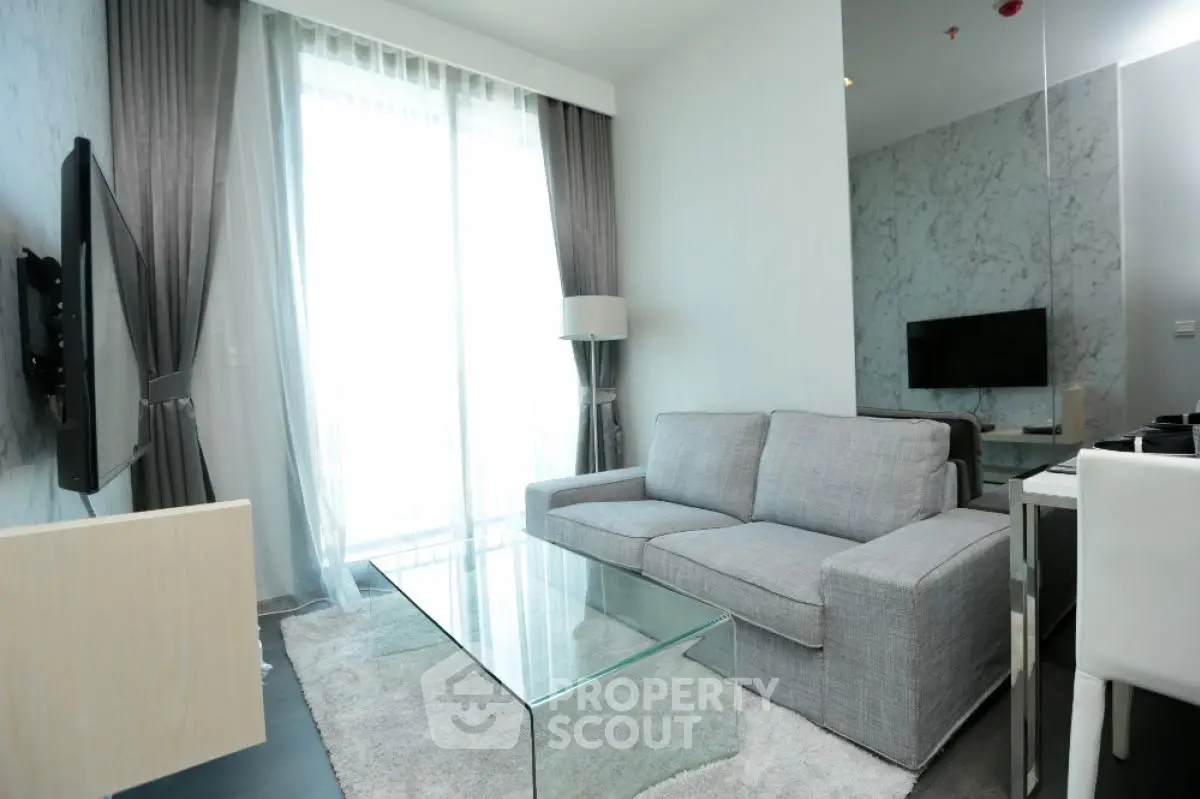 Modern living room with sleek gray sofa and glass coffee table, featuring floor-to-ceiling windows.