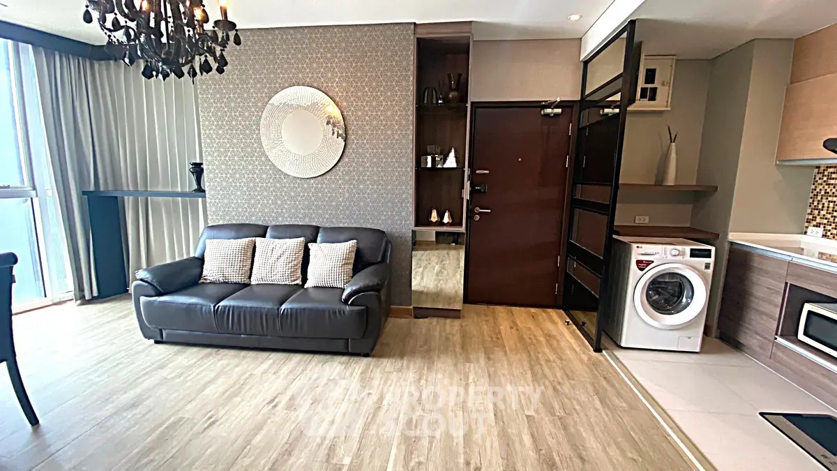Modern living room with elegant decor and in-unit washer, featuring stylish chandelier and open kitchen layout.