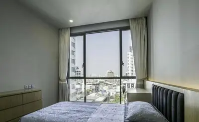 Modern bedroom with large window offering city view in high-rise apartment.