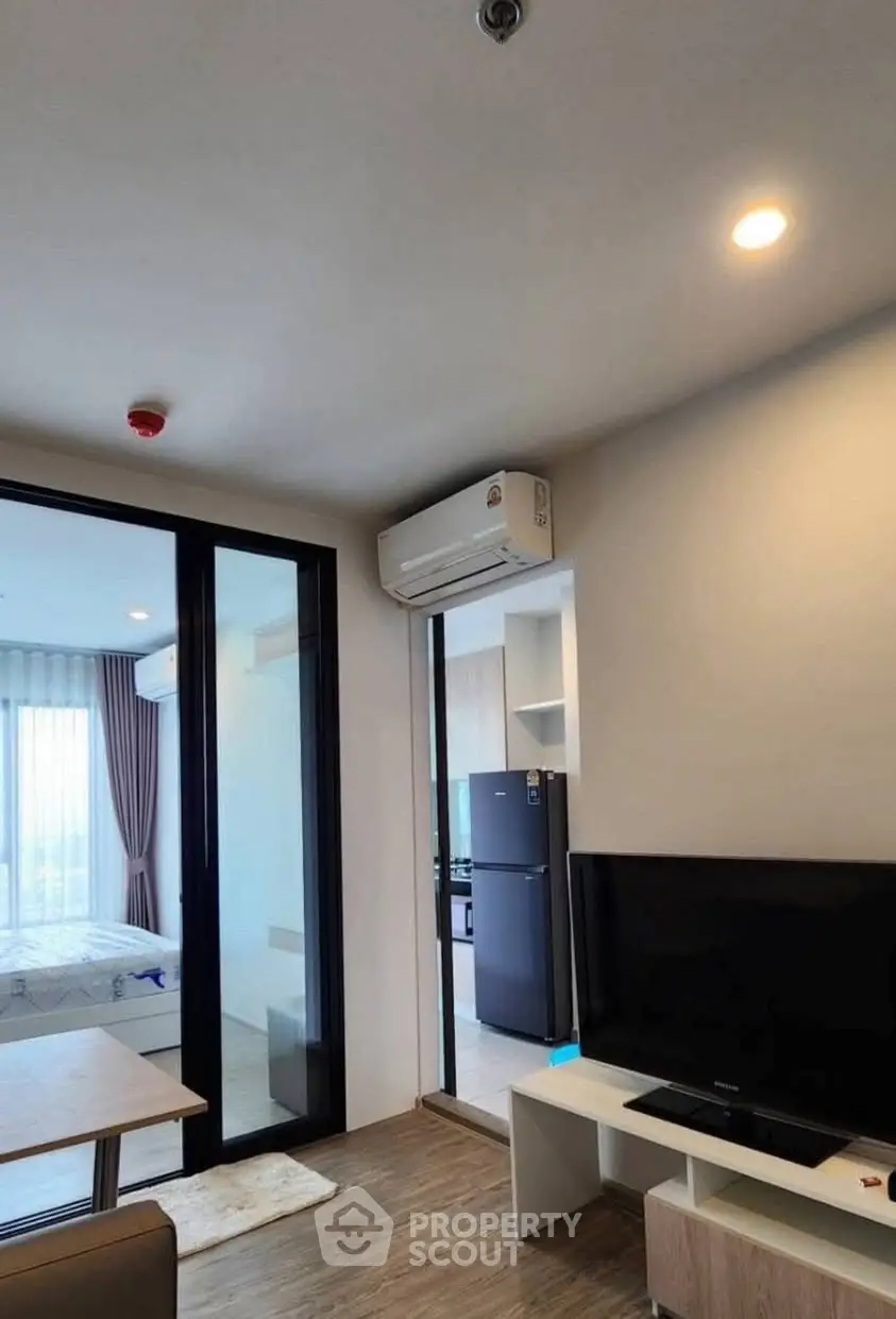 Modern living room with TV, air conditioning, and view into bedroom and kitchen.