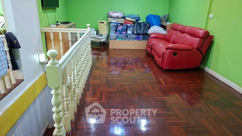 Spacious living area with polished wooden floors and vibrant green walls, featuring a red leather sofa.